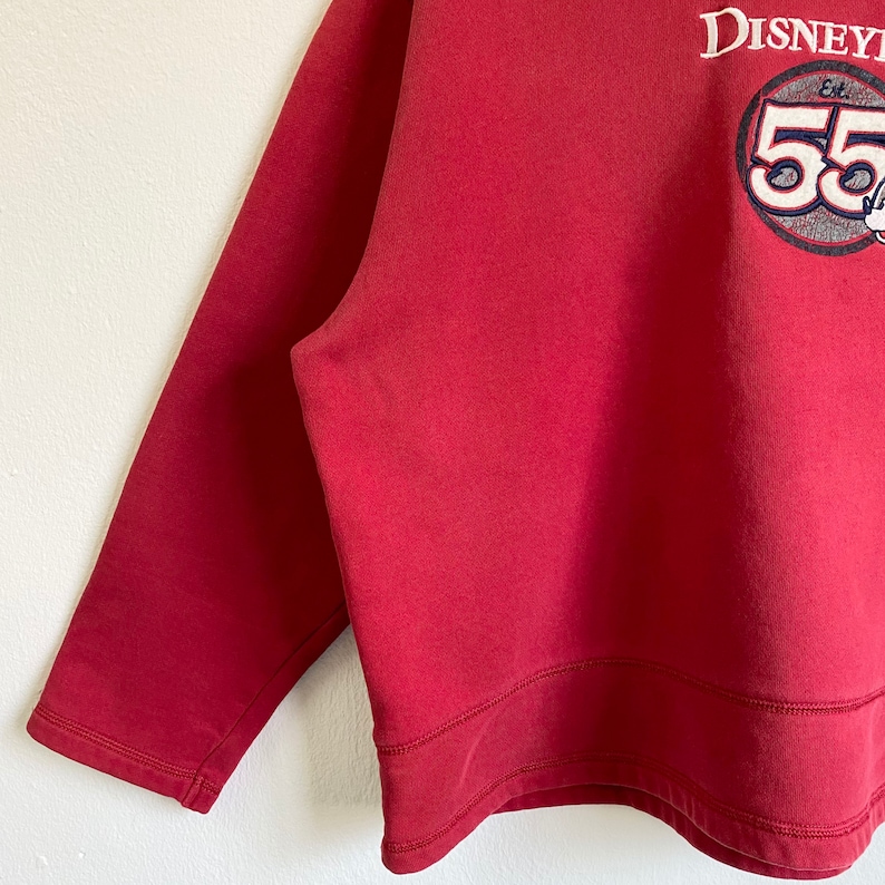 May include: Red long-sleeve sweatshirt with a white embroidered logo that says "Disney" and "Est. 55" with a Mickey Mouse head graphic.