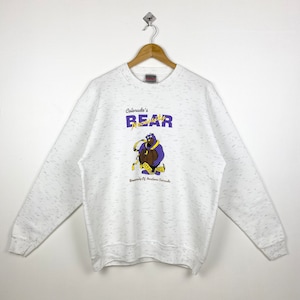 May include: White sweatshirt with a graphic of a purple bear holding a barrel with the text "Colorado's Necessity BEAR" and "University of Northern Colorado" printed below.