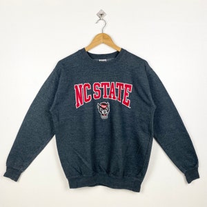 May include: A dark gray sweatshirt with a red and white NC STATE logo and a wolf mascot.