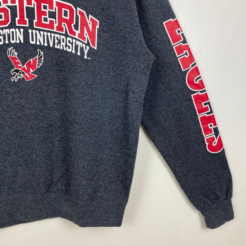May include: A dark grey sweatshirt with the words "Western Washington University" and a red eagle logo on the front. The right sleeve has the word "Eagles" in red letters.