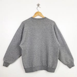 Puede incluir: Una sudadera gris con mangas largas y cuello redondo.