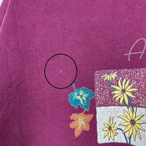 May include: A maroon t-shirt with a floral design and the word "Autumn" printed on the front.