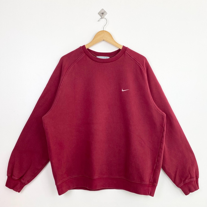 May include: A red crew neck sweatshirt with a white Nike swoosh logo on the left chest.