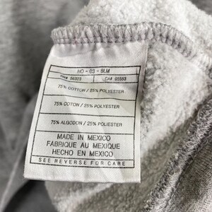 May include: Close-up of a gray fabric tag with black text. The tag reads "HO-03-BLM", "RN# 56323", "CA# 05553", and "75% COTTON / 25% POLYESTER". The tag also states "MADE IN MEXICO" and "SEE REVERSE FOR CARE".
