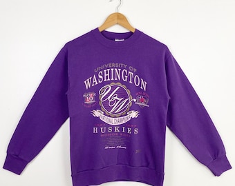 Op de afbeelding: Paarse trui met een vintage logo van de University of Washington Huskies. Het logo toont de initialen van de school "UW" in een cirkel met de woorden "National Champions" en "Huskies Honor Roll" eronder.