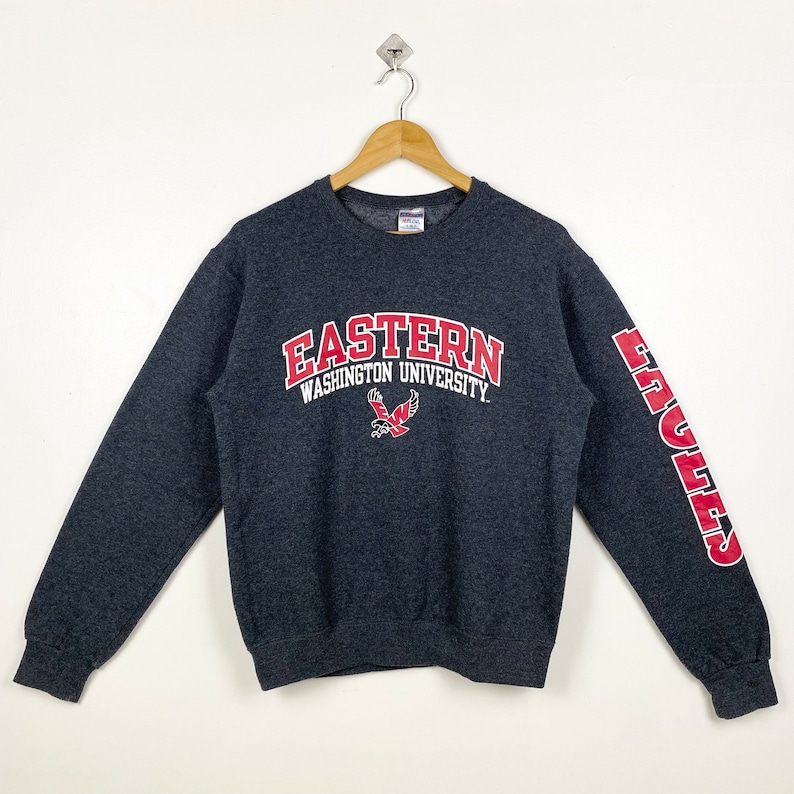May include: Grey sweatshirt with red lettering that reads "Eastern Washington University" and a red eagle logo. The right sleeve has the word "Eagles" in red lettering.