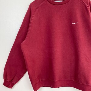 May include: A red long-sleeved sweatshirt with a white Nike swoosh logo on the left chest.