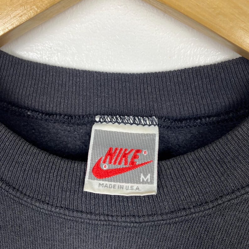 May include: A black Nike sweatshirt with a white tag that says "NIKE" in red with a white checkmark and "MADE IN U.S.A." in black. The tag also has a size "M" in black.