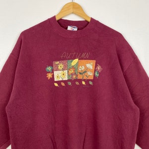 May include: A maroon sweatshirt with a graphic of autumn leaves and flowers. The text "AUTUMN" is printed above the graphic.