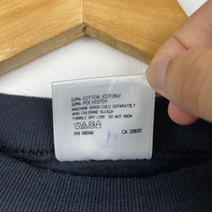 May include: White care label with black text detailing the fabric content and care instructions for a garment. The label reads: 50% Cotton (Coton)/ 50% Polyester Machine Wash Cold Separately Non Chlorine Bleach Tumble Dry Low Do Not Iron RN 68046 CA 20832