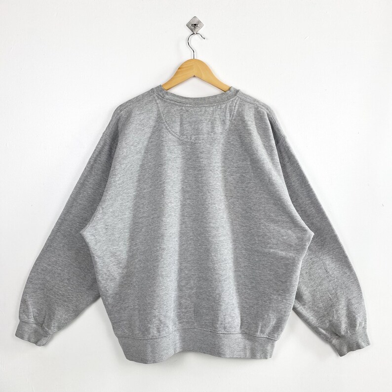 May include: A heather gray sweatshirt hangs on a wooden hanger against a white background. The crew neck sweatshirt has long sleeves and a ribbed hem and cuffs. The back of the sweatshirt is visible, showing the neckline and shoulder seams.