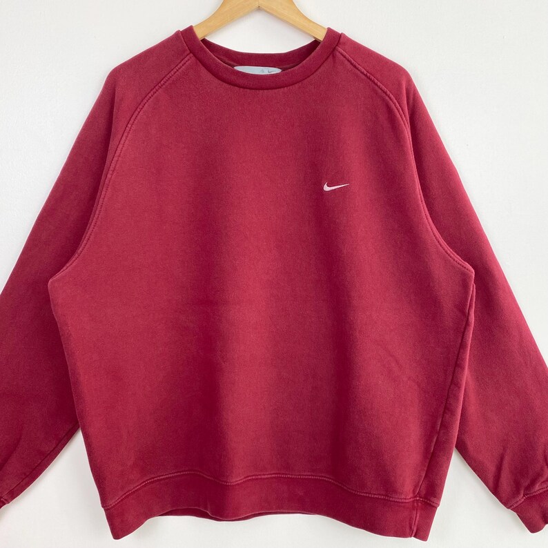 May include: A red crew neck sweatshirt with a white Nike swoosh logo on the left chest.
