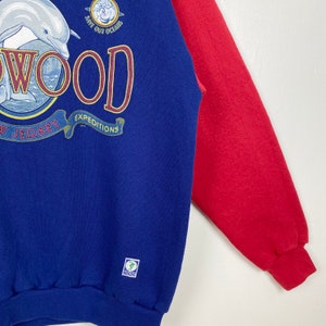 May include: Blue and red sweatshirt with a dolphin and the text "WOOD" in a circle with the text "EXPEDITIONS" and "NEW JERSEY" below. The text "SAVE OUR OCEANS" is above the circle. The sweatshirt has a green label with the text "INSCUS".
