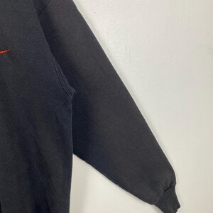 May include: A black sweatshirt with a red logo on the front. The sweatshirt has long sleeves and a ribbed cuff.