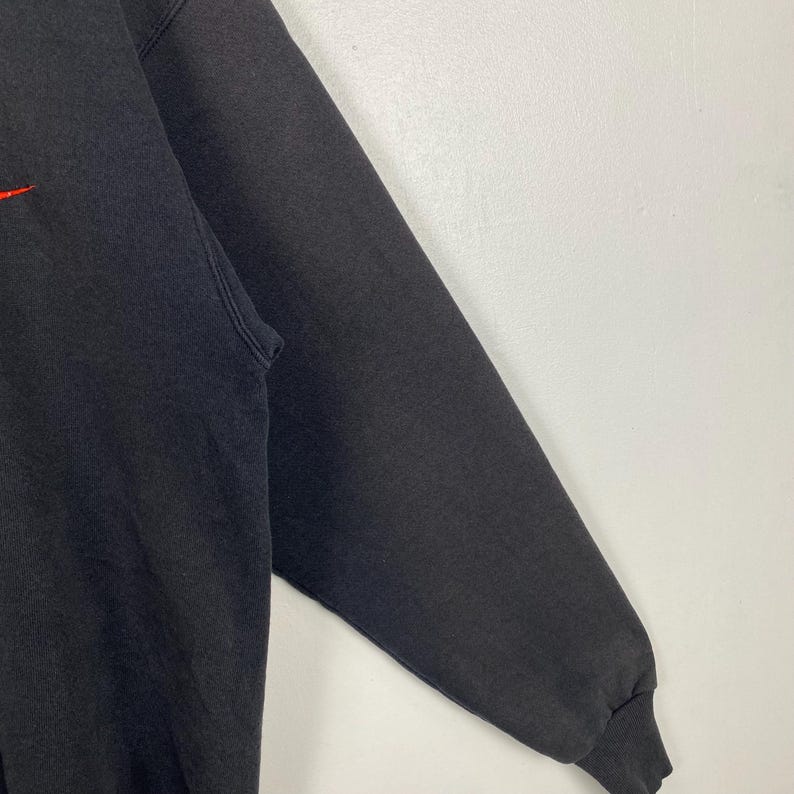 May include: A black sweatshirt with a red logo on the front. The sweatshirt has long sleeves and a ribbed cuff.