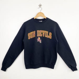 Op de afbeelding: Zwart sweatshirt met een "Sun Devils" logo in bordeauxrood en goud en een cartoon mascotte.