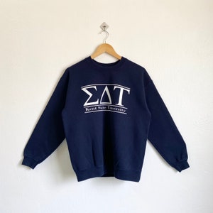 Może przedstawiać: Granatowa bluza z białym nadrukiem greckich liter i tekstem "ΣΔΤ Kent State University".