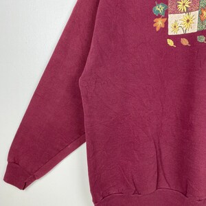 May include: A maroon sweatshirt with a colorful autumn-themed print featuring leaves and flowers.