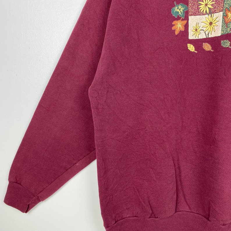 May include: A maroon sweatshirt with a colorful autumn-themed print featuring leaves and flowers.