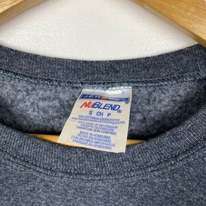 May include: A grey sweatshirt tag with the text "NUBLEND" in a white box with a black border. The tag also includes the text "S CH P" and the following information: "50% Cotton/Algod&oacute;n/Cotton 50% Polyester/Poli&eacute;ster/Polyester Exclusive of Decoration Excepto Decoraci&oacute;n Garniture Non Comprise Made in Honduras Hecho en Honduras Con Insumos Importados Fabrique au Honduras"