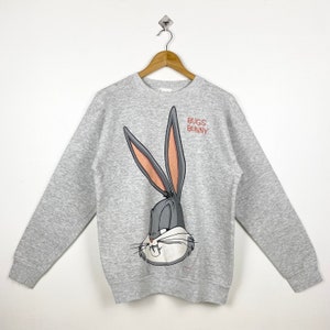 May include: A grey sweatshirt featuring a large Bugs Bunny graphic on the front. The graphic depicts Bugs Bunny's face and ears, with the text "Bugs Bunny" above it.
