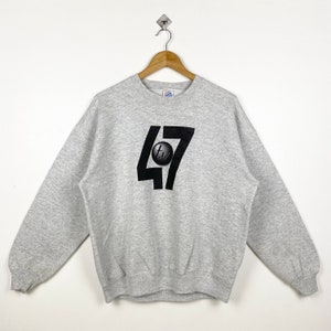 May include: A gray sweatshirt with a black graphic of the number 47 with a circle containing the letters "tv" inside the 7.