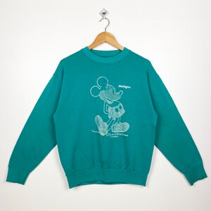 Puede incluir: Una sudadera de color azul turquesa con un gráfico blanco de Mickey Mouse y el texto "Washington" impreso en la parte delantera. La sudadera está hecha de un material suave y cómodo.