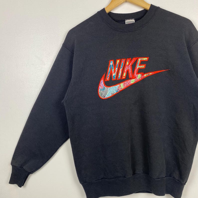 May include: Black sweatshirt with a large, colorful embroidered Nike logo. The logo is red, pink, blue, and green.