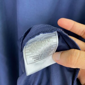 May include: Close-up of a navy blue garment tag. The tag is white with black text, listing fabric composition as 55% polyester and 45% nylon, and 55% polyester and 45% polyamide. The tag also includes the text "FABRIQUE EN THAILANDE" and "MADE IN THAILAND".