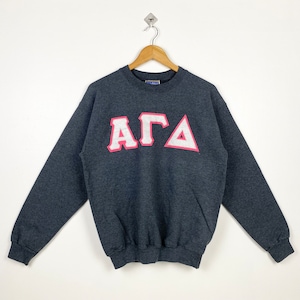 May include: A grey sweatshirt with a pink and white "AGA" logo on the front.
