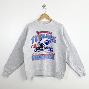 Pode incluir: Camisola cinzenta com um logotipo dos Tennessee Titans em azul e vermelho e o texto "Tennessee Titans AFC Conference Champions".