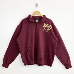May include: A maroon Champion sweatshirt with a quarter-zip collar and a kangaroo pocket. The sweatshirt features the text "MORRIS" above a logo and the word "Cougars" in gold lettering.