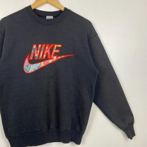 May include: Black sweatshirt with a large red and white Nike logo with a colorful floral pattern. The logo says "NIKE" in red letters.