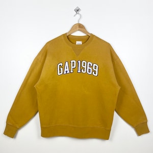 May include: A mustard yellow sweatshirt with a navy blue and white embroidered logo that reads "GAP 1969".