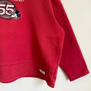 May include: Red sweatshirt with a Mickey Mouse graphic and the text "Est. 55" on the front. The sweatshirt has a ribbed hem and cuffs.