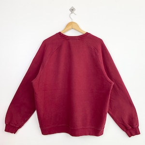 May include: A maroon crew neck sweatshirt with long sleeves and a ribbed hem.