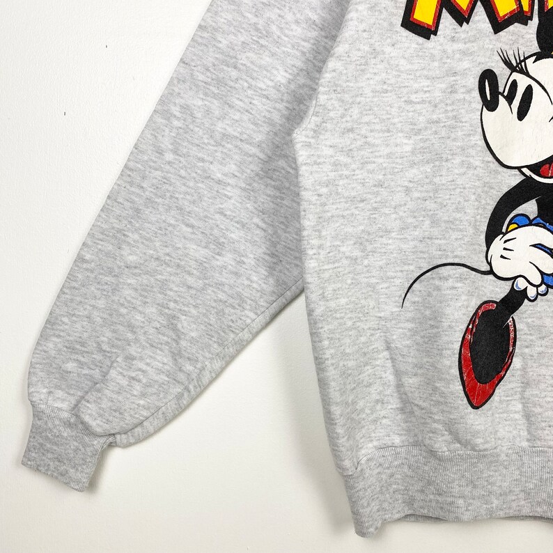 K&ouml;nnte beinhalten: Grauer Sweatshirt mit einem Cartoon-Bild von Minnie Mouse in einem roten Kleid und schwarzen Schuhen. Der Text "Runaway" ist in gelben Buchstaben auf dem Sweatshirt gedruckt.