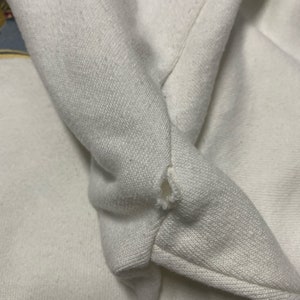 Może przedstawiać: Zbliżenie na białą bawełnianą bluzę z małą dziurką w materiale.