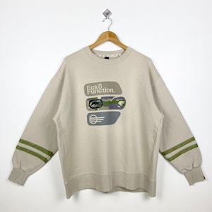 May include: A beige sweatshirt with long sleeves and green stripes on the cuffs. The front of the sweatshirt features a graphic print of the words "Ecko Function" and a camouflage pattern.