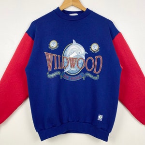 May include: Blue and red sweatshirt with a dolphin graphic and the text "WILDWOOD" with the words "ADVENTURE", "EXPEDITIONS" and "NEW JERSEY" underneath.