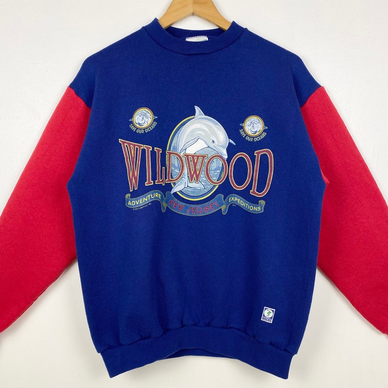 May include: Blue and red sweatshirt with a dolphin graphic and the text "WILDWOOD" with the words "ADVENTURE", "EXPEDITIONS" and "NEW JERSEY" underneath.