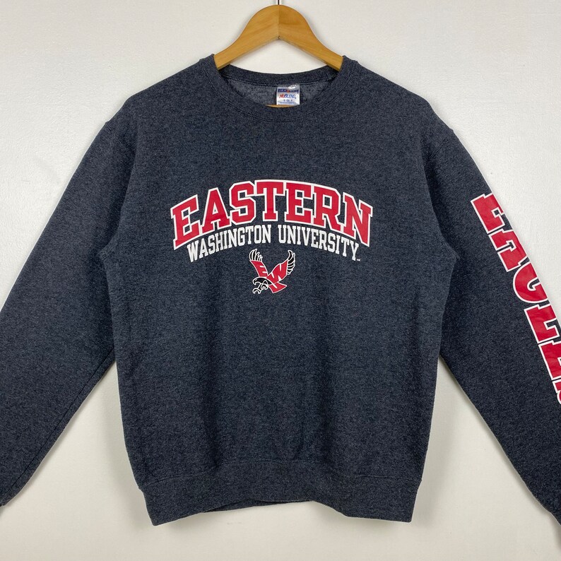 May include: A grey sweatshirt with the words "Eastern Washington University" in red and white lettering. The university's mascot, an eagle, is also printed on the front of the sweatshirt. The word "Eagles" is printed in red on the right sleeve.