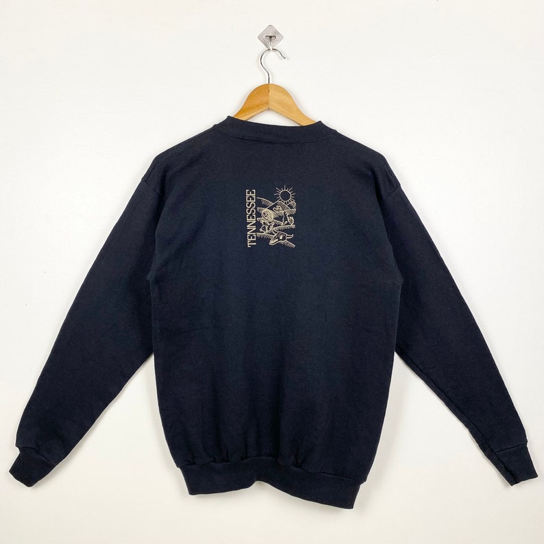 May include: Black long-sleeve sweatshirt with a gold graphic of a sun, mountains, and the word "TENNESSEE" on the back.