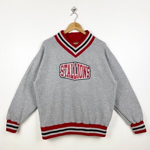 May include: Gray sweatshirt with a red and black striped collar and cuffs. The sweatshirt has a red "STALLIONS" logo on the front.