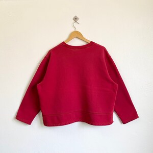 May include: A red long-sleeved sweatshirt with a crew neck and a slightly cropped hem.