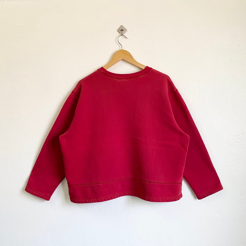 May include: A red long-sleeved sweatshirt with a crew neck and a slightly cropped hem.