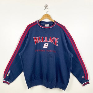 May include: A blue sweatshirt with red and white stripes on the sleeves. The sweatshirt has the text "WALLACE 2 PENSKE RACING" embroidered on the front.