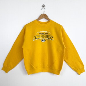 May include: Yellow sweatshirt with a Green Bay Packers logo. The logo is a green and white football with the words "Green Bay Packers" and "NFC North" printed on it.