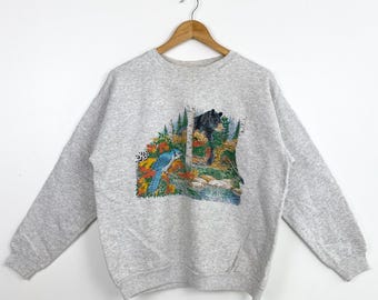 May include: A grey sweatshirt with a colourful print of a blue jay, a black bear, and a forest scene.