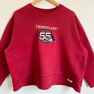 May include: Red Disneyland sweatshirt with a vintage Mickey Mouse logo and the text "Disneyland Est. 55" embroidered on the front.